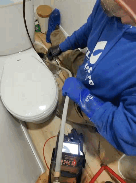 Technicien débouchant un drain principal par la toilette à l'aide d'un câble mécanique dans une résidence à Montréal.
