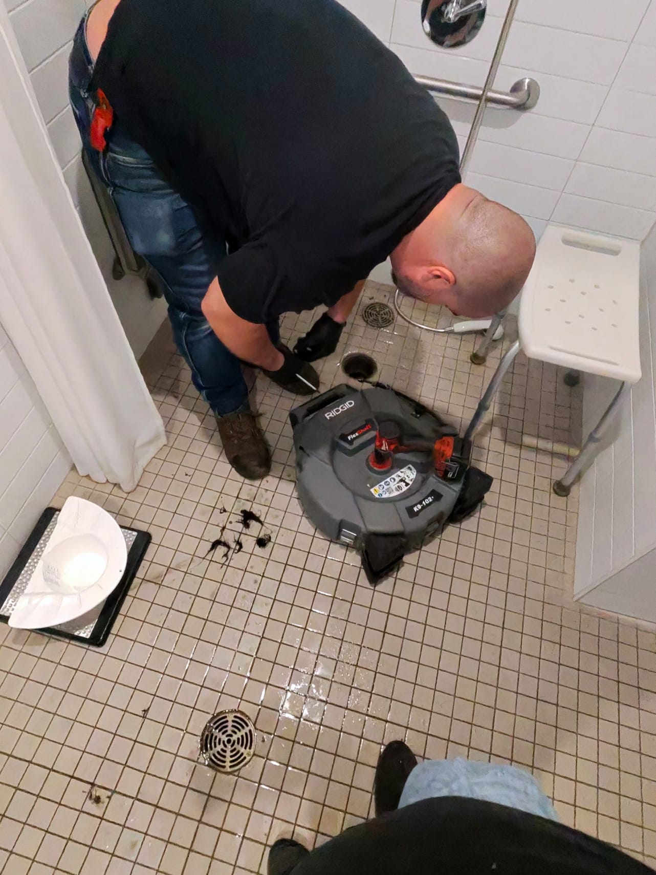 Technicien effectuant un débouchage de drain de douche avec une machine RIDGID dans une salle de bain à Montréal.