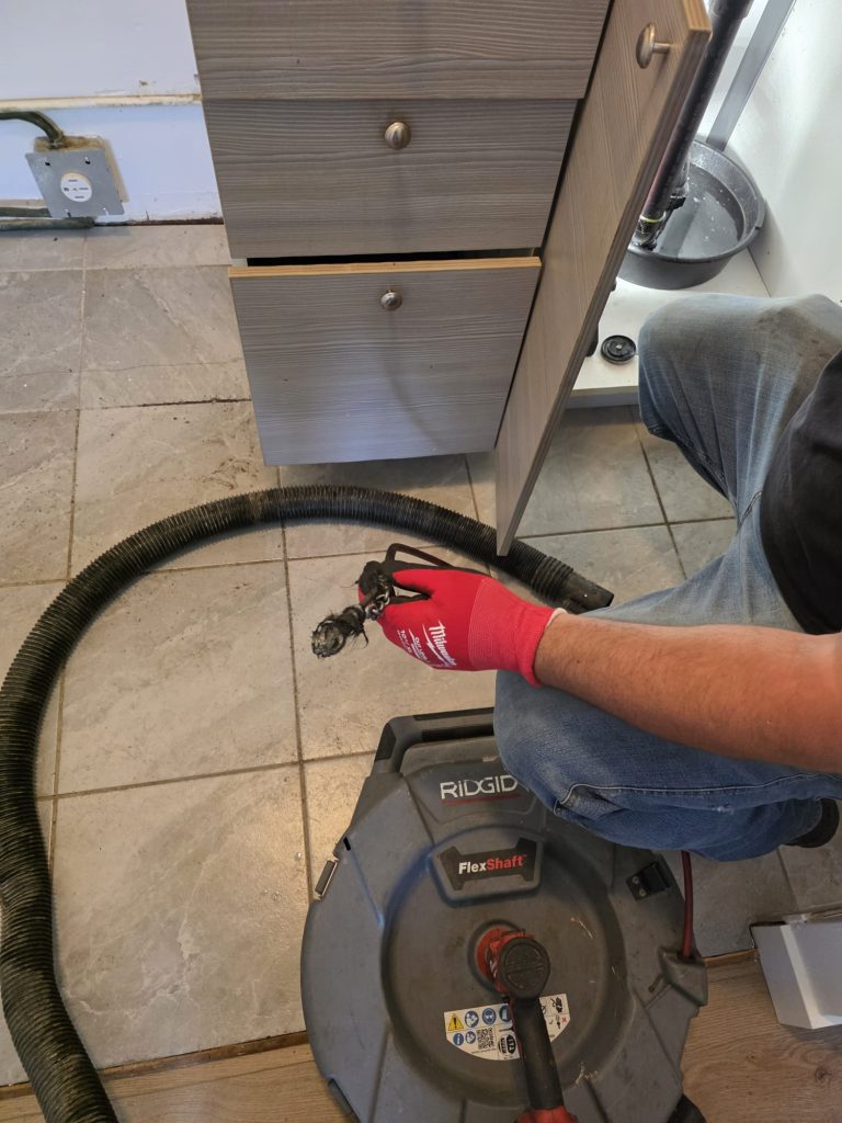 Mechanical drain cleaning tool and removed deposits beneath a kitchen sink.