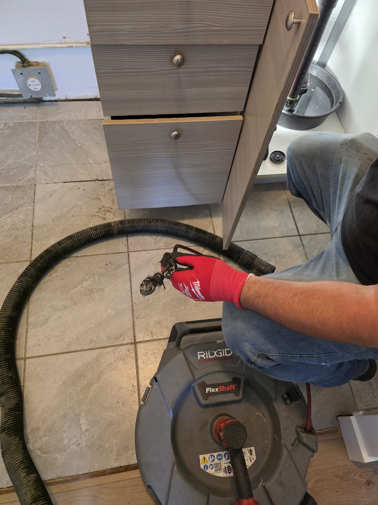 Technicien de Flow Pro Drain utilisant une machine RIDGID FlexShaft pour nettoyer une conduite sous un meuble de lavabo.