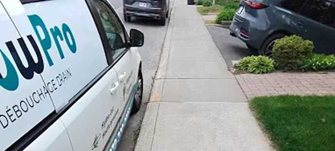 A white drain cleaning service van parked next to a sidewalk in a residential neighborhood.